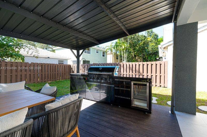 9963 NW 2nd Court, Plantation, FL 33324 Covered patio featuring a wood-finish deck and an outdoor kitchen equipped with a stainless steel grill and a built-in beverage refrigerator, enclosed by a privacy fence