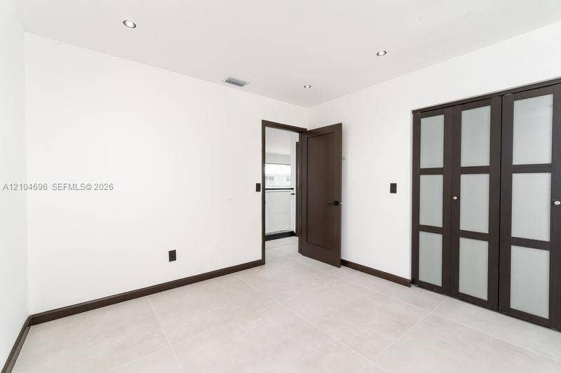 9963 NW 2nd Court, Plantation, FL 33324 Interior space featuring light-toned tile flooring, recessed ceiling lighting, a dark-finish interior door, and a built-in closet with frosted glass panels