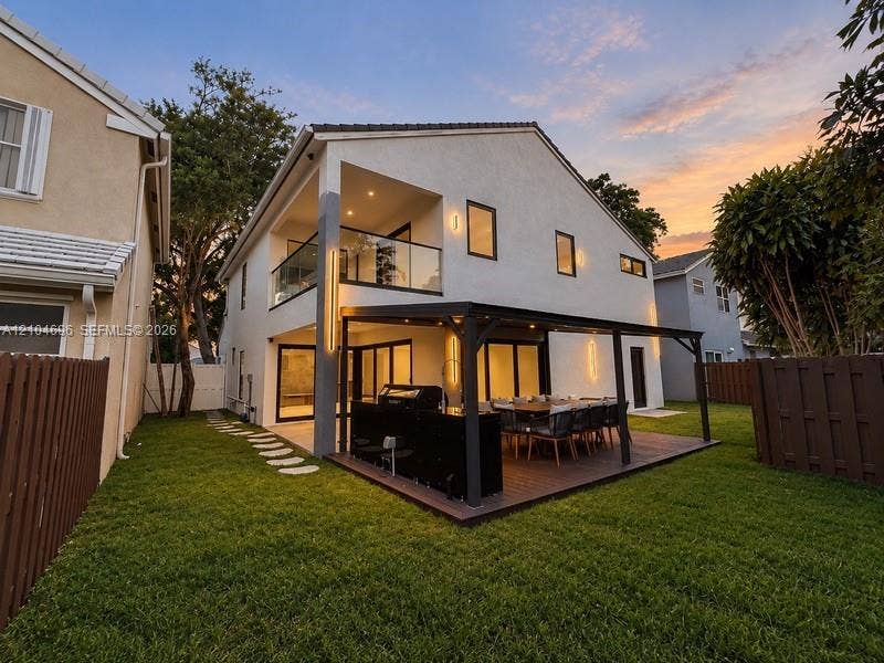 9963 NW 2nd Court, Plantation, FL 33324 Exterior features include a stucco finish, covered deck with a pergola, built-in outdoor kitchen, second-story balcony with glass railing, and a fenced yard