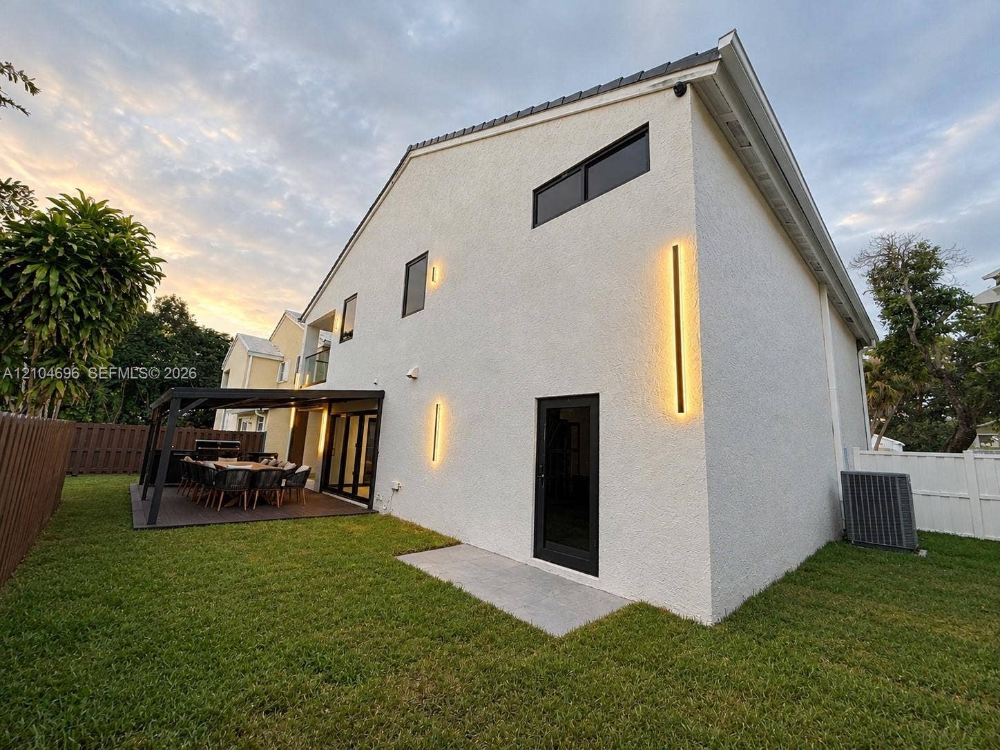 9963 NW 2nd Court, Plantation, FL 33324 Stucco exterior featuring vertical linear wall sconces, a covered patio with dark-finish decking, and black-trimmed windows and doors