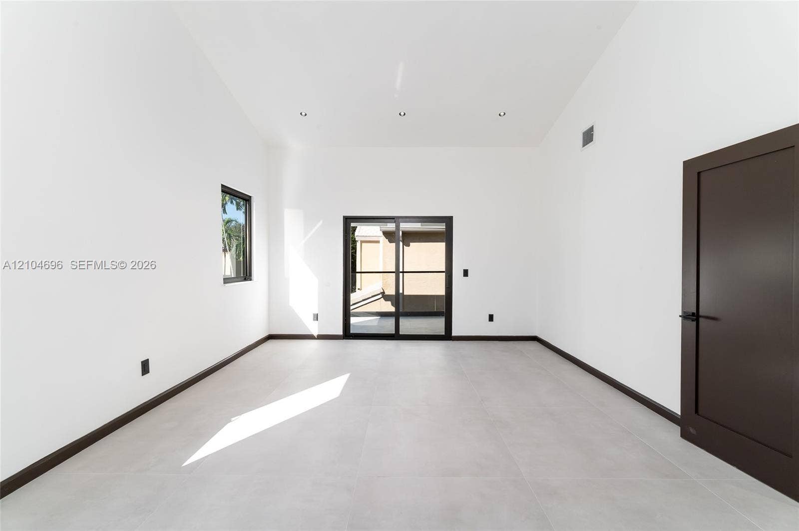9963 NW 2nd Court, Plantation, FL 33324 High-ceiling interior featuring large-format tile flooring, recessed lighting, dark-framed sliding glass doors, and a solid-core door with matte black hardware