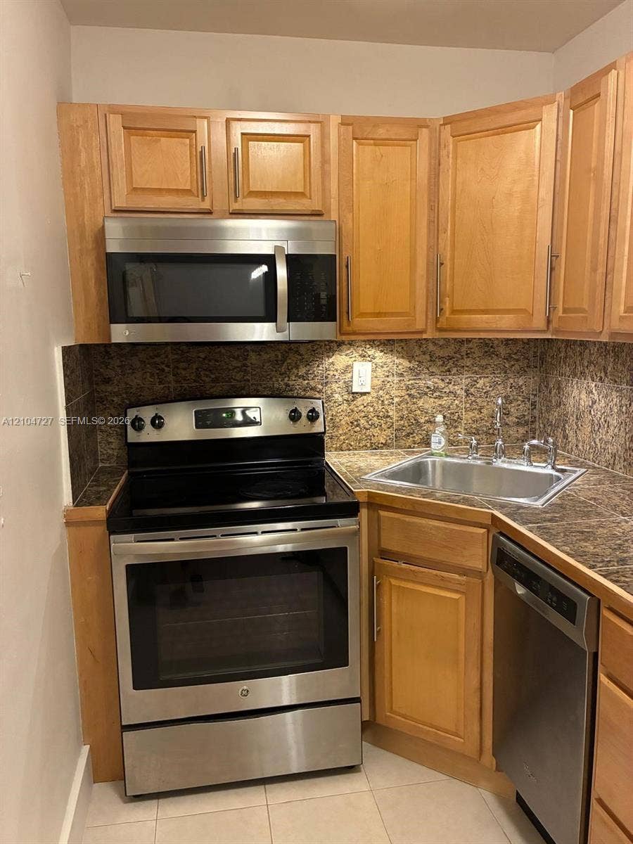 1955 NE 135th Street, #206, North Miami, North Miami, FL 33181 Kitchen featuring light-finish cabinetry, stone-surfaced countertops, tiled backsplash, and a suite of stainless steel appliances including a built-in microwave, range, and dishwasher