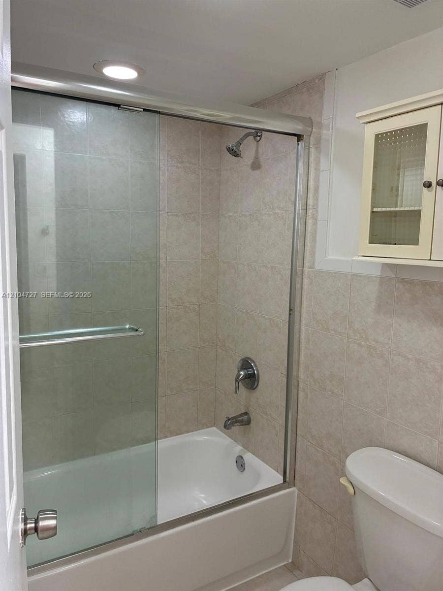 1955 NE 135th Street, #206, North Miami, North Miami, FL 33181 Bathtub and shower combination featuring a sliding glass enclosure, neutral tile surround, recessed lighting, and built-in upper wall cabinetry
