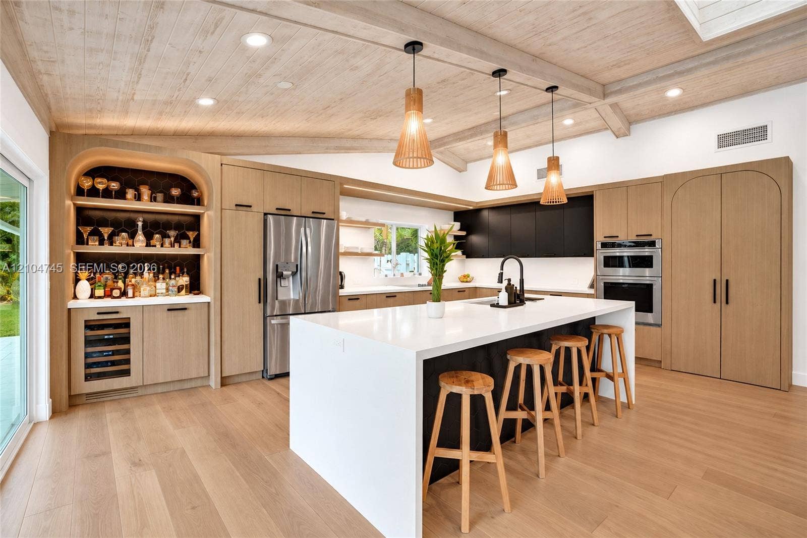 Vaulted wood-finish ceiling with exposed beams, wood-finish flooring, stainless steel appliances, built-in shelving with integrated lighting, and a kitchen island with a white countertop