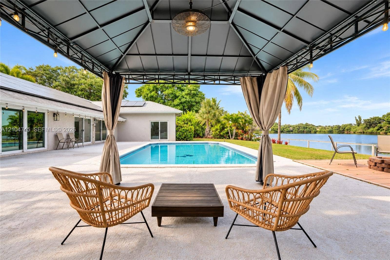 Outdoor covered patio with string lighting, expansive pool area, and direct water frontage