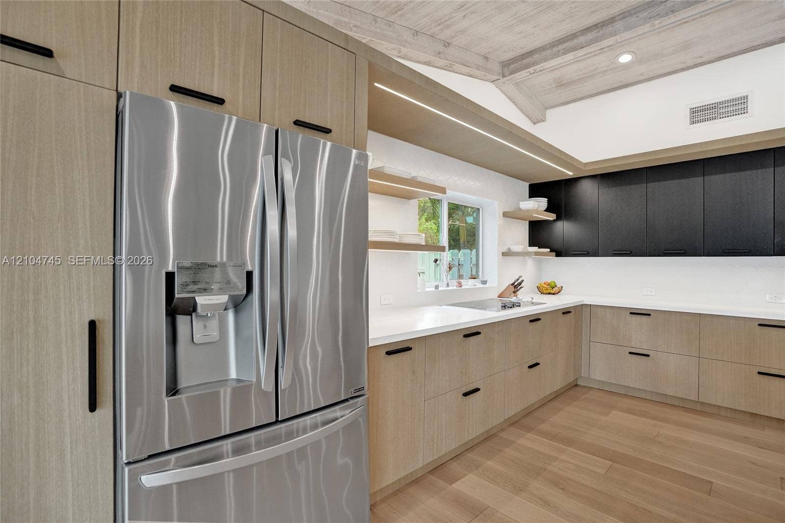 Stainless steel French door refrigerator, light wood-finish cabinetry, dark upper cabinetry, white countertops, and light wood-finish flooring