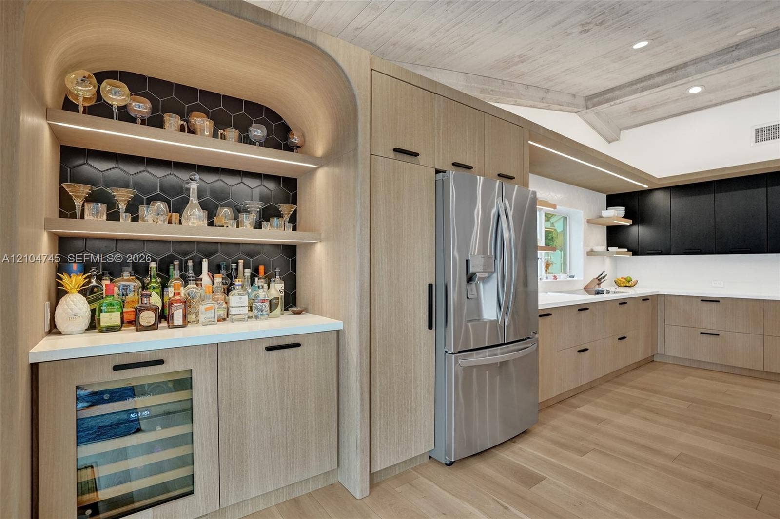 Kitchen featuring light wood-finish flooring, light wood-finish cabinetry, stainless steel refrigerator, white countertops, and a built-in bar area with hexagonal tile backsplash and beverage cooler
