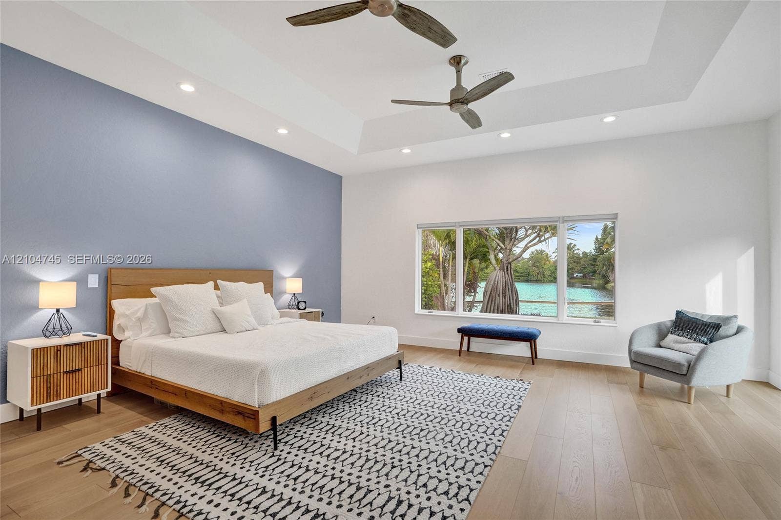 Tray ceiling with recessed lighting, wood-finish flooring, accent wall, ceiling fans, and large window overlooking a body of water