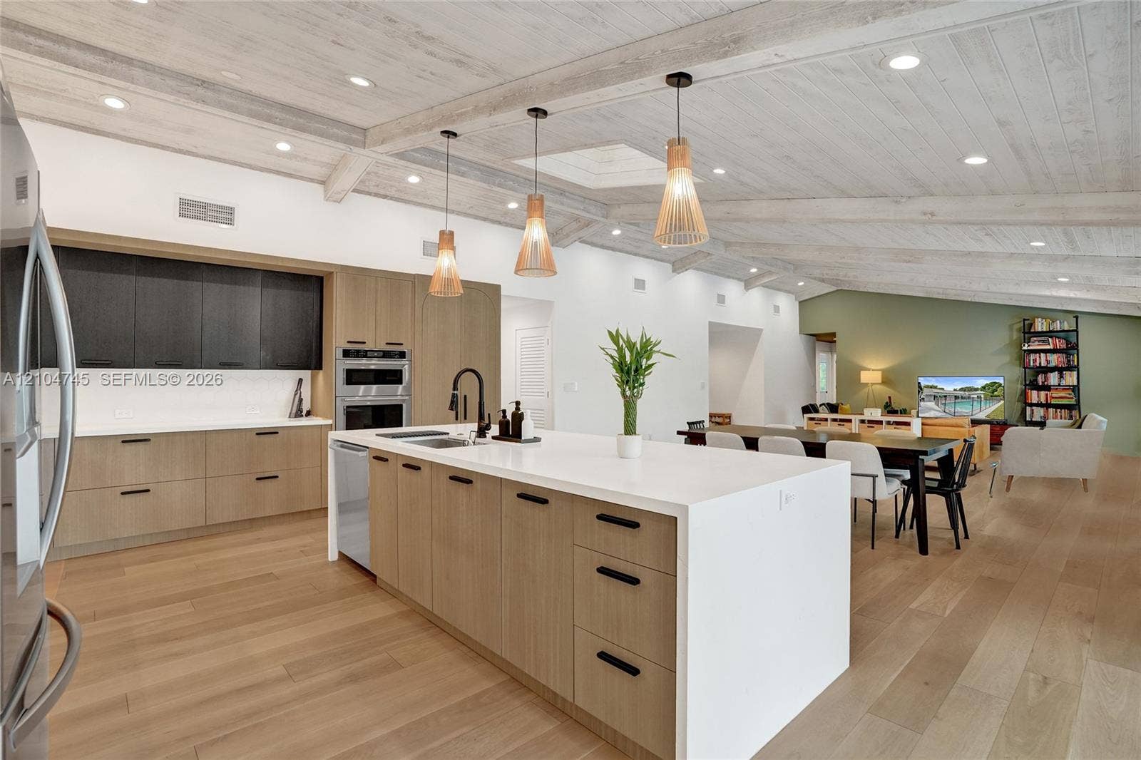 Open-concept kitchen featuring an expansive island with a white countertop, wood-finish cabinetry, and built-in stainless steel appliances