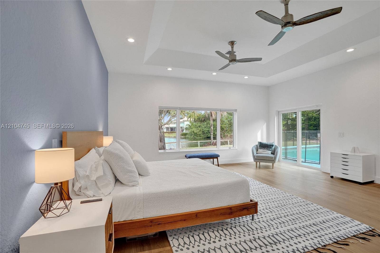 Tray ceiling with recessed lighting and two ceiling fans, wood-finish flooring, and a sliding glass door to the exterior