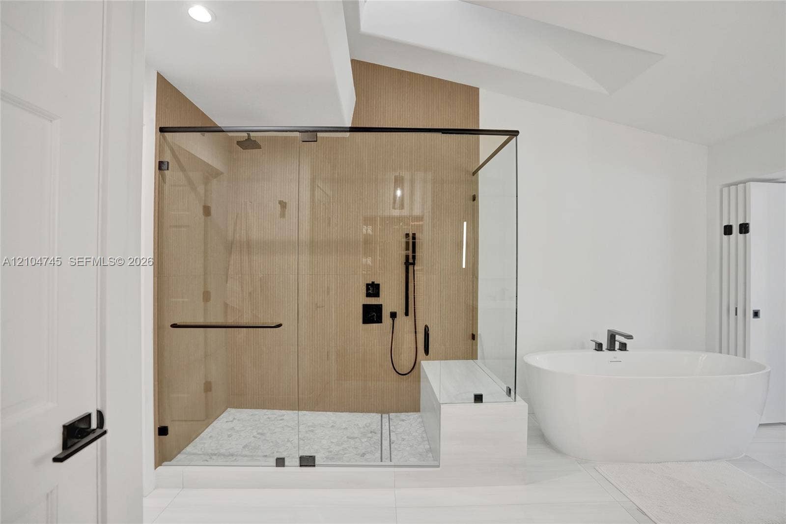 Spacious shower enclosure with glass panels, light wood-finish wall, and black fixtures