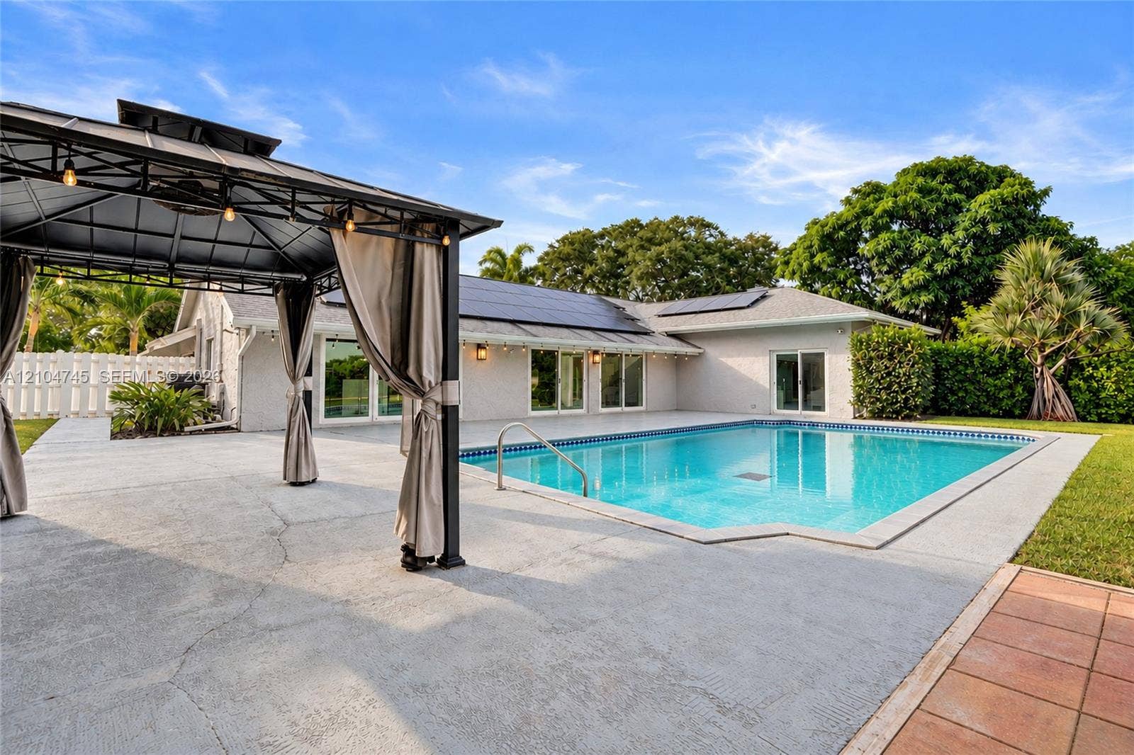 Rear exterior featuring a swimming pool, expansive concrete patio, and a covered gazebo