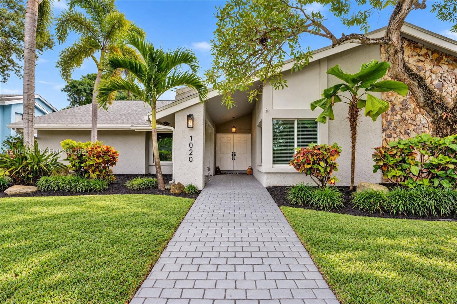 White stucco exterior with stone accents, featuring a gray paver walkway