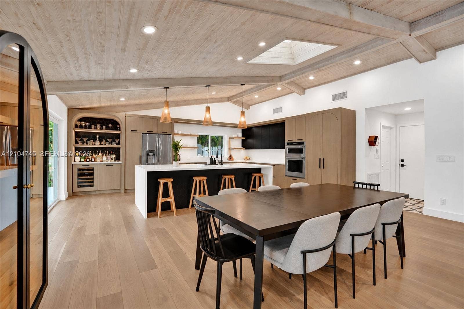 Vaulted wood-finish ceiling with exposed beams, wood-finish flooring, custom built-in bar, center island with stone countertop, and integrated stainless steel appliances