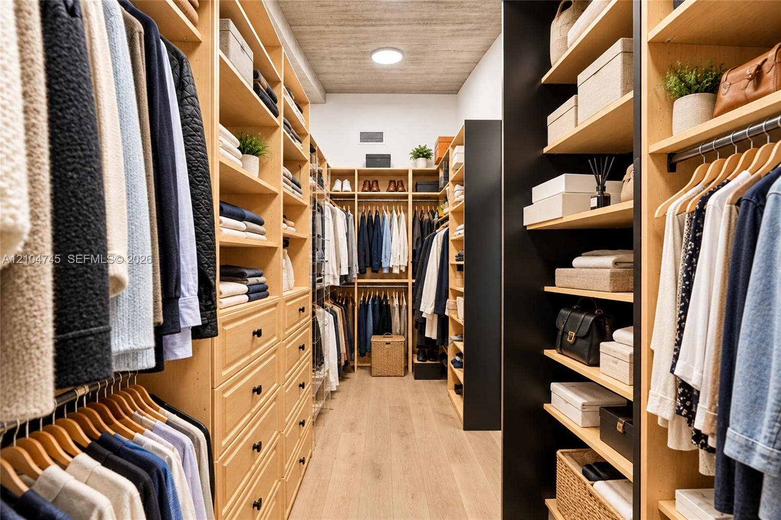Walk-in closet featuring extensive built-in shelving, multiple hanging rods, integrated drawers with dark hardware, and light wood-finish flooring