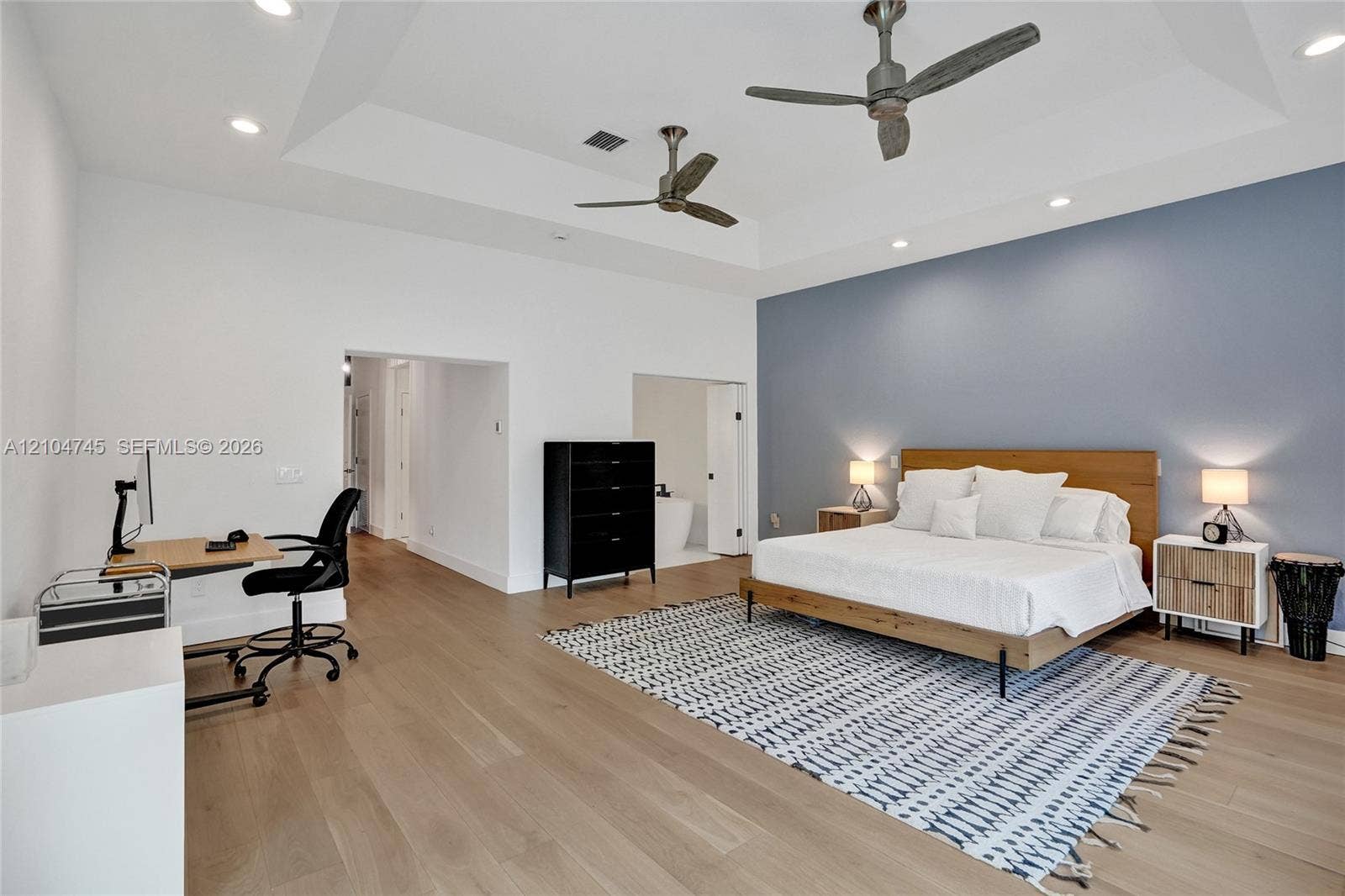 Tray ceiling with recessed lighting, two ceiling fans, wood-finish flooring, and a distinct accent wall