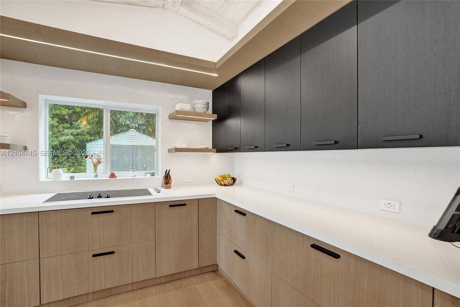 Modern kitchen featuring wood-finish lower cabinetry, dark-finish upper cabinetry, white countertops, and a white hexagonal tile backsplash