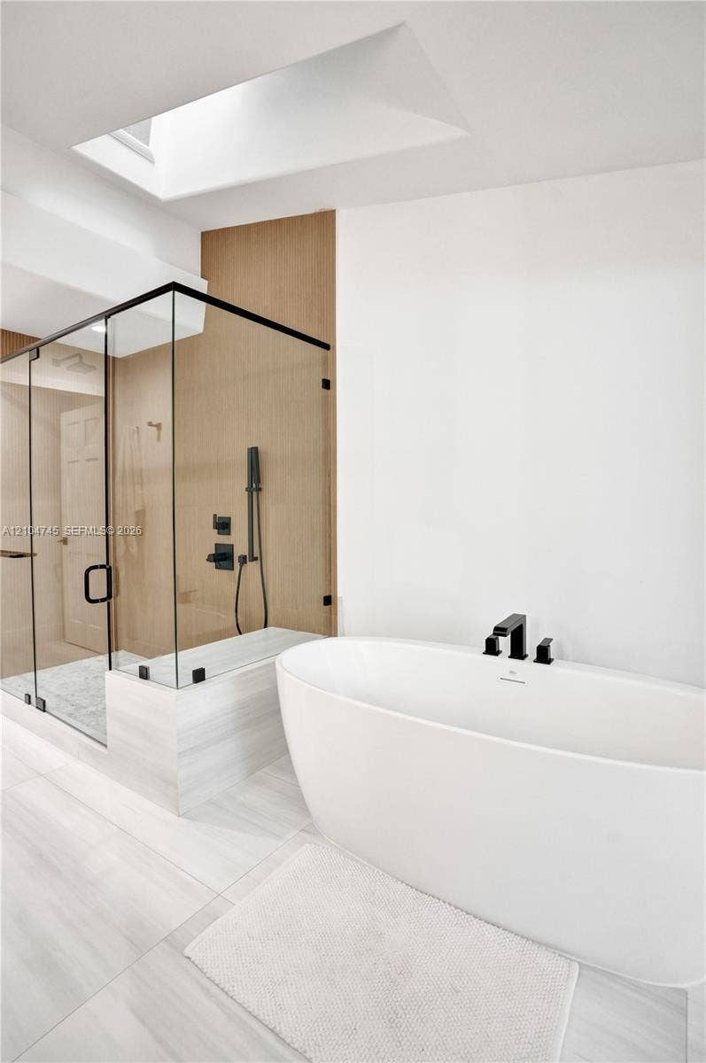 Freestanding soaking tub with matte black fixtures, glass-enclosed shower with matte black shower system, and skylight