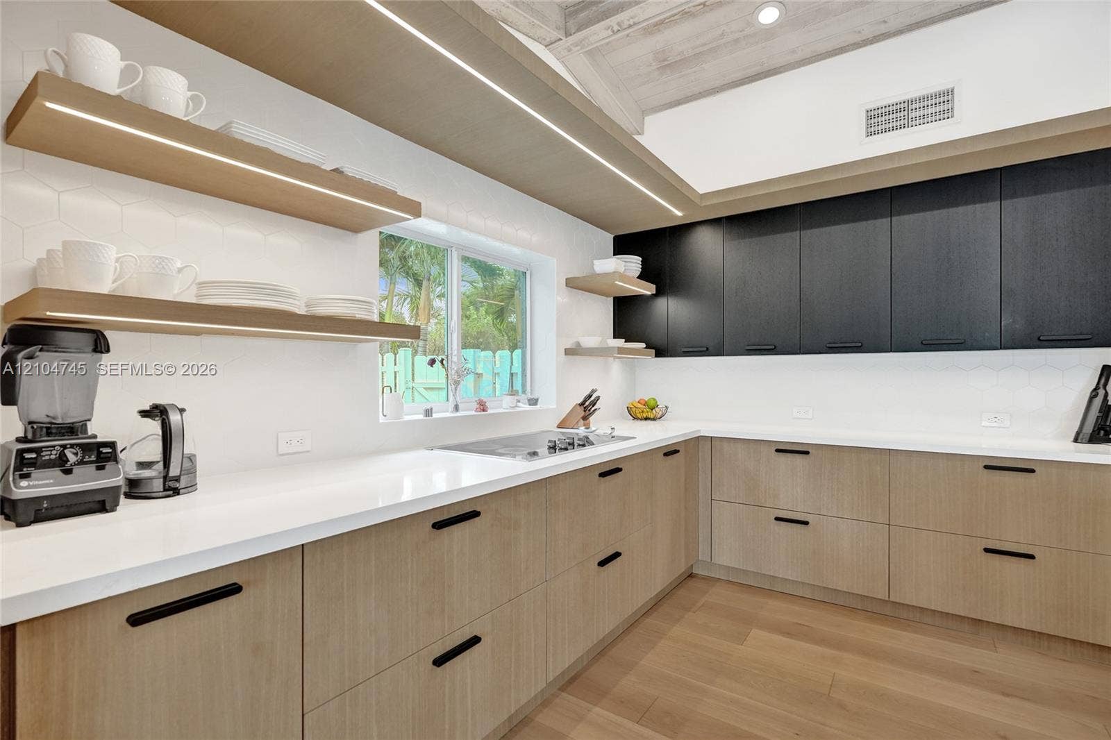 Contemporary kitchen featuring light wood-finish cabinetry, dark upper cabinetry, white countertops, and a hexagon tile backsplash