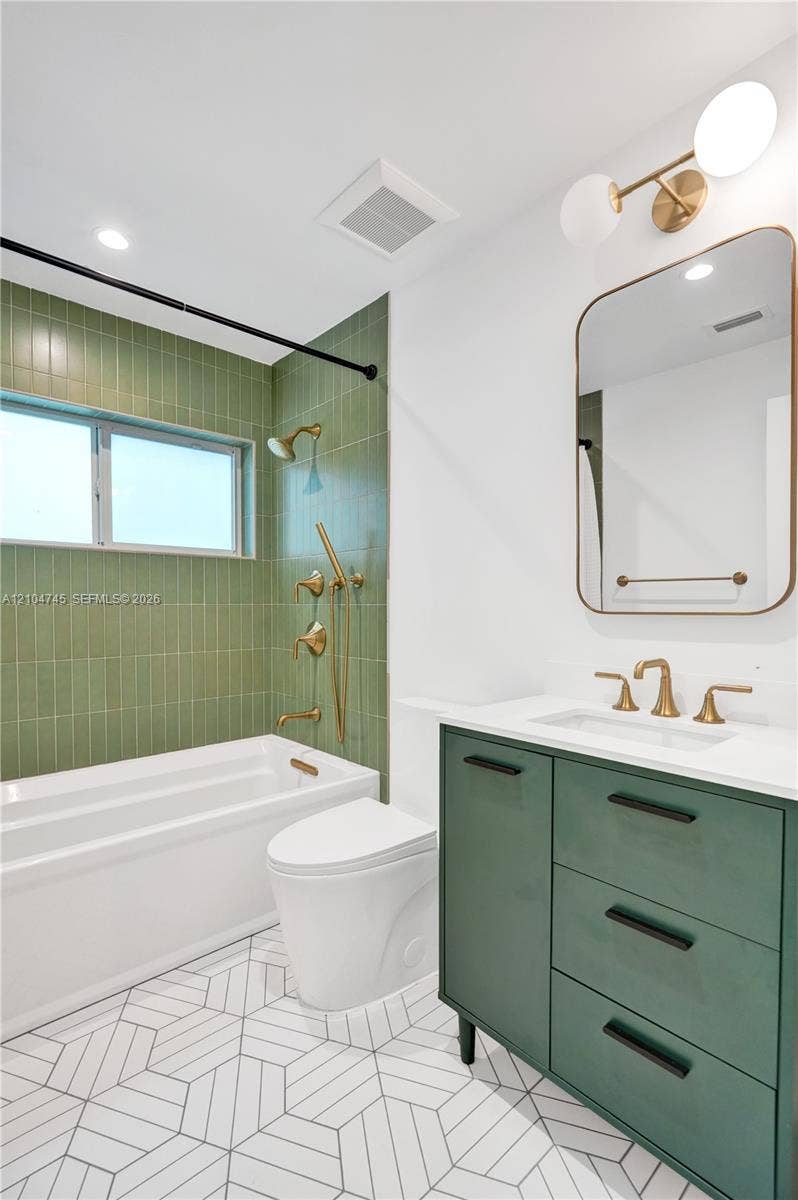 Bathtub with brass-finish fixtures, green subway tile surround, and geometric floor tiling