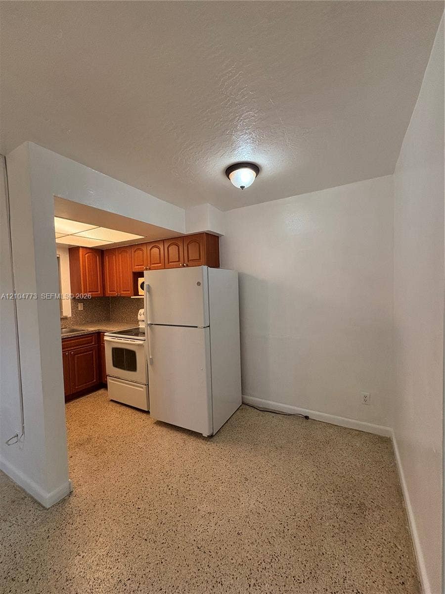 Kitchen with wood-finish cabinetry, tile backsplash, and white appliances