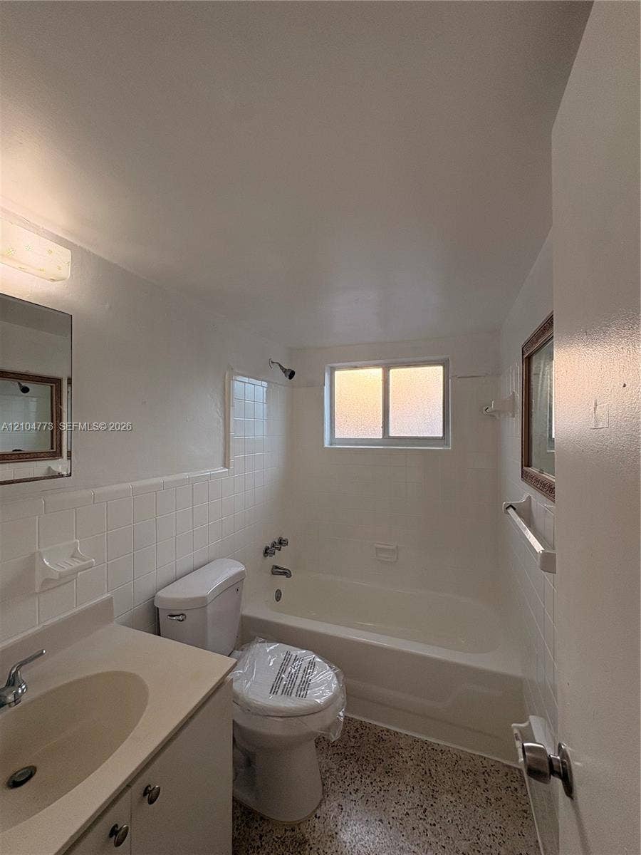 Bathroom featuring a single vanity, integrated sink, and white ceramic tile tub surround