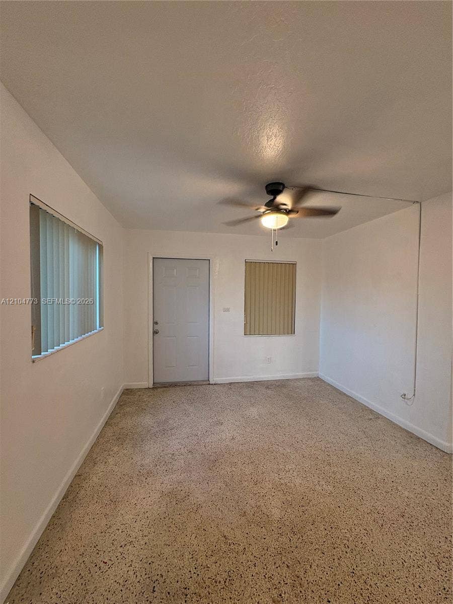 Neutral wall paint with textured flooring, a ceiling fan with integrated lighting, and horizontal blinds