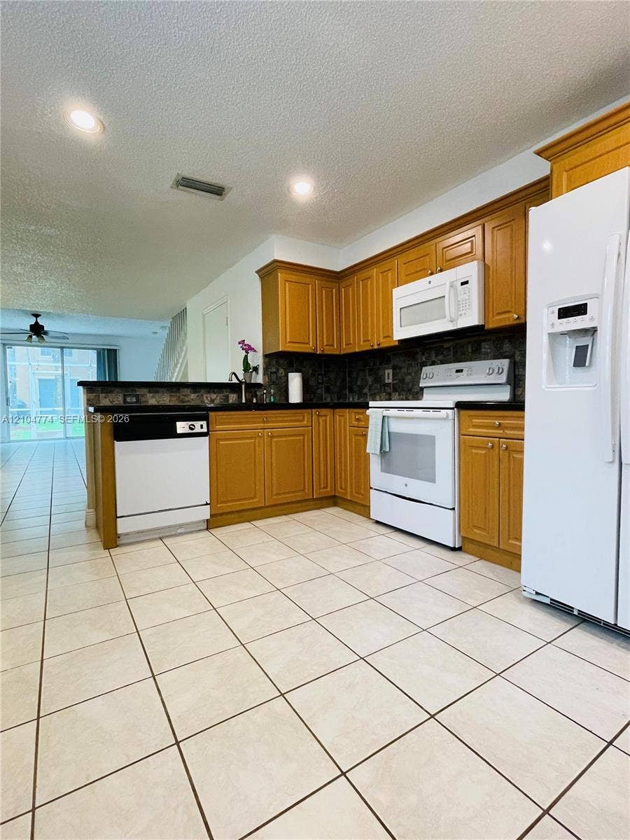 1503 Veracruz Lane, #5-14, Weston, Weston, FL 33327 Kitchen featuring wood cabinetry, dark stone-style countertops, recessed ceiling lighting, a tiled backsplash, and light-colored tile flooring