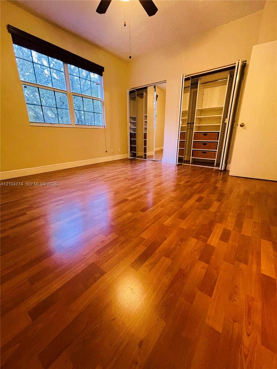 1503 Veracruz Lane, #5-14, Weston, Weston, FL 33327 Room featuring wood-finish flooring, dual mirrored-door closets with built-in shelving and drawers, a multi-pane window, and a ceiling-mounted fan