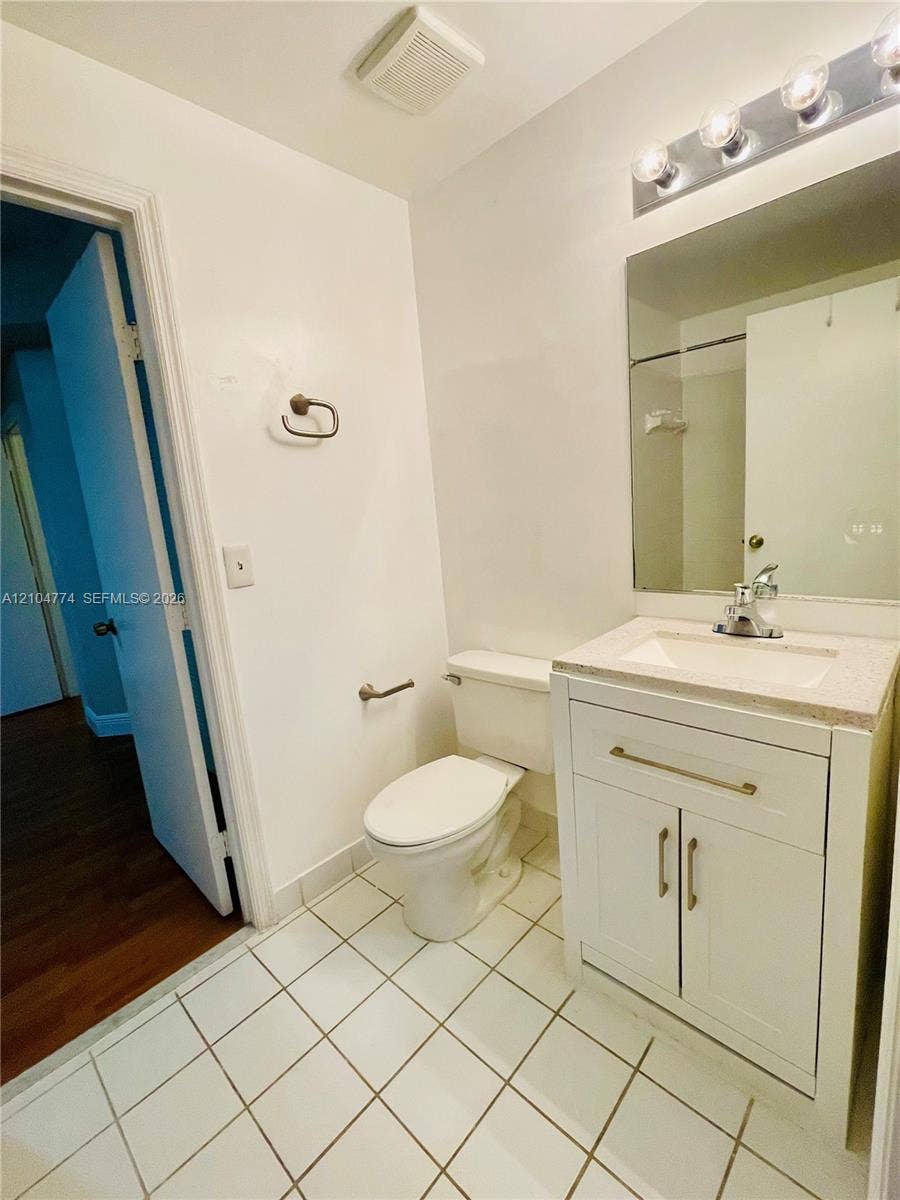 1503 Veracruz Lane, #5-14, Weston, Weston, FL 33327 White vanity cabinet with a stone-composite countertop, integrated sink, and modern metallic hardware, paired with a multi-bulb vanity light fixture and ceramic floor tiling