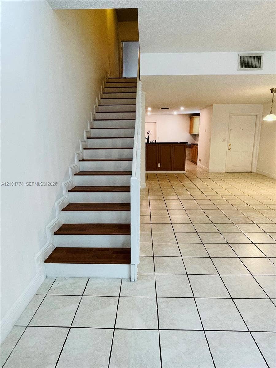 1503 Veracruz Lane, #5-14, Weston, Weston, FL 33327 Staircase featuring wood-finish treads and white risers, square ceramic tile flooring, and a kitchen peninsula with dark-toned cabinetry
