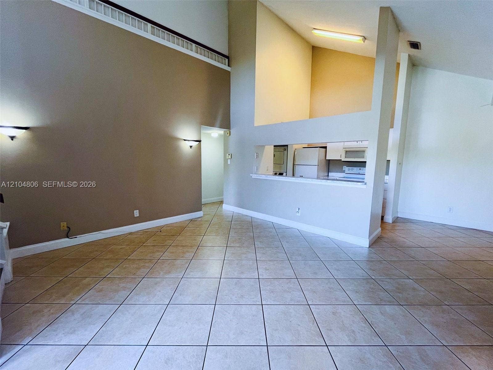 10451 SW 157th Place, #303, Miami, FL 33196 Vaulted ceilings, tiled flooring, built-in sconce lighting, and a partial wall opening to the kitchen area
