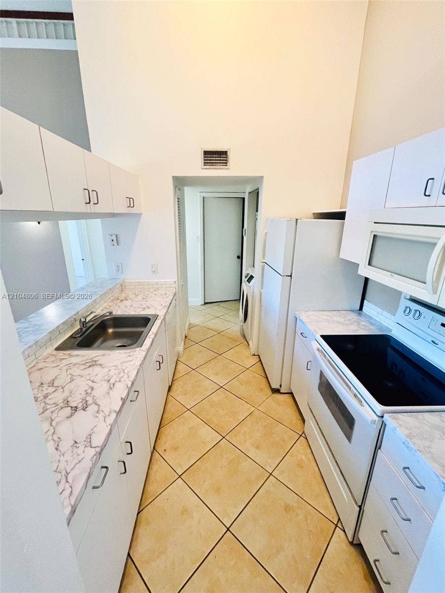 10451 SW 157th Place, #303, Miami, FL 33196 Kitchen featuring diagonal tile flooring, white cabinetry, a stainless steel sink, and light-colored countertops