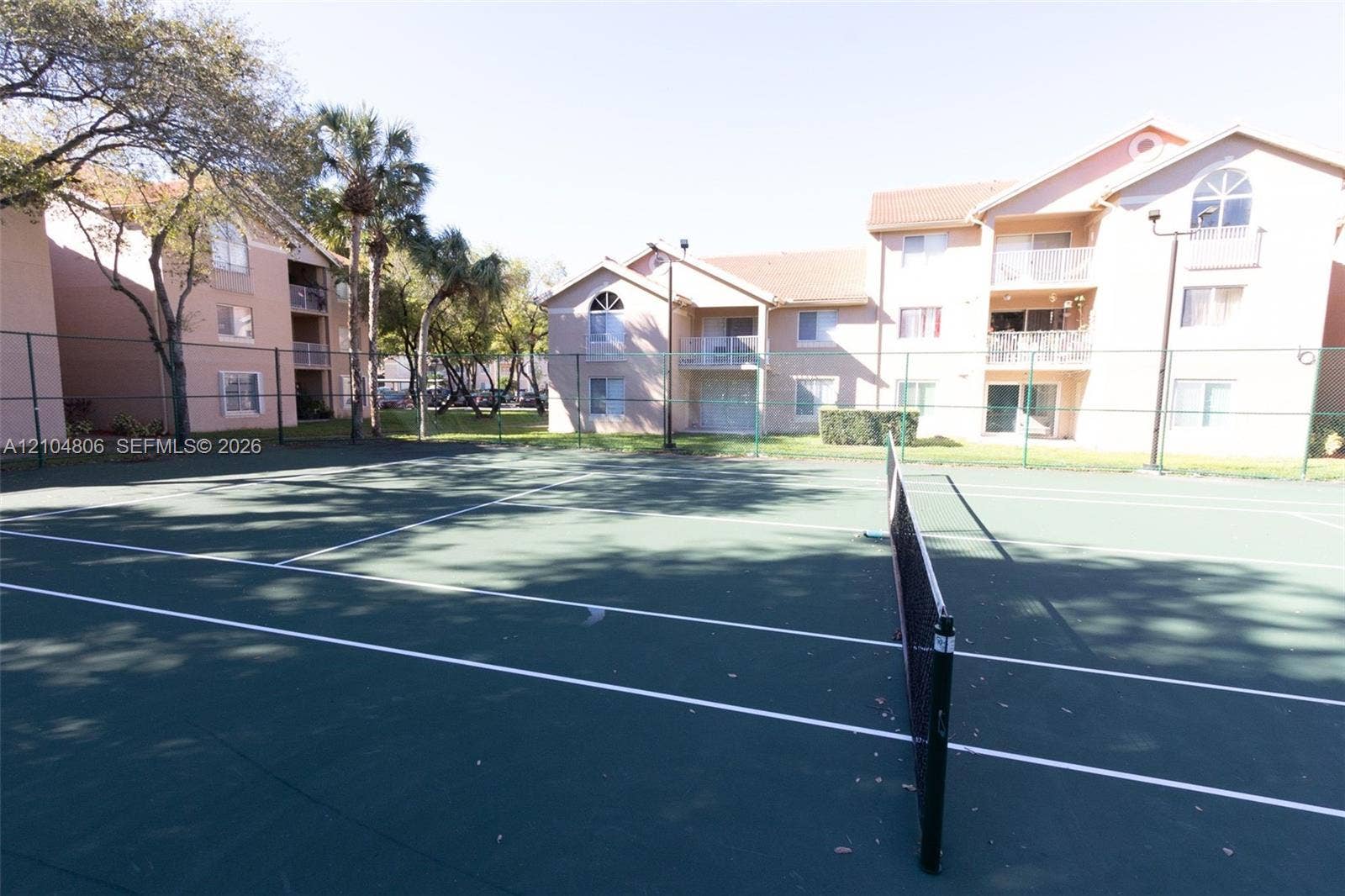 10451 SW 157th Place, #303, Miami, FL 33196 Hardcourt tennis court with net, surrounded by fencing and mature trees
