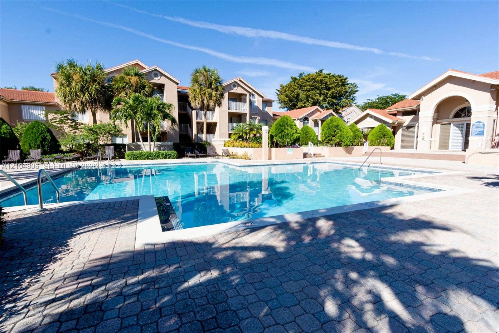 10451 SW 157th Place, #303, Miami, FL 33196 Expansive outdoor swimming pool with surrounding paver decking, adjacent to multi-story buildings with balconies, and palm trees