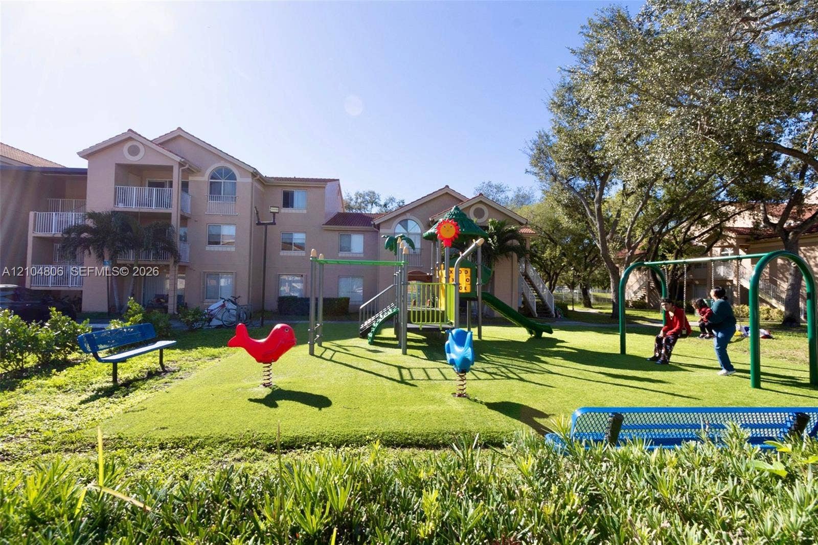 10451 SW 157th Place, #303, Miami, FL 33196 Outdoor playground featuring a swing set, slide structure, and spring riders on a green turf surface