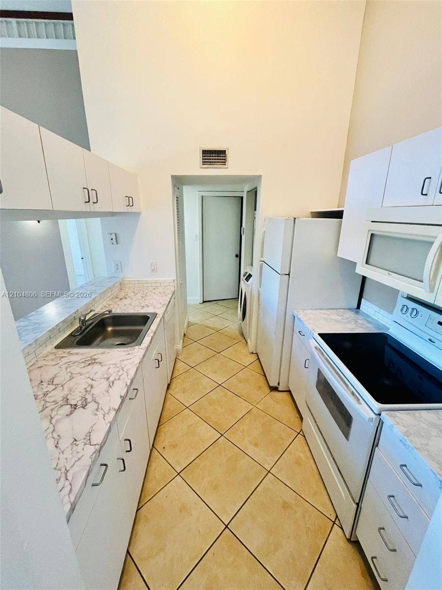 10451 SW 157th Place, #303, Miami, FL 33196 Kitchen featuring white cabinetry, a stainless steel sink, patterned countertops, and tile flooring