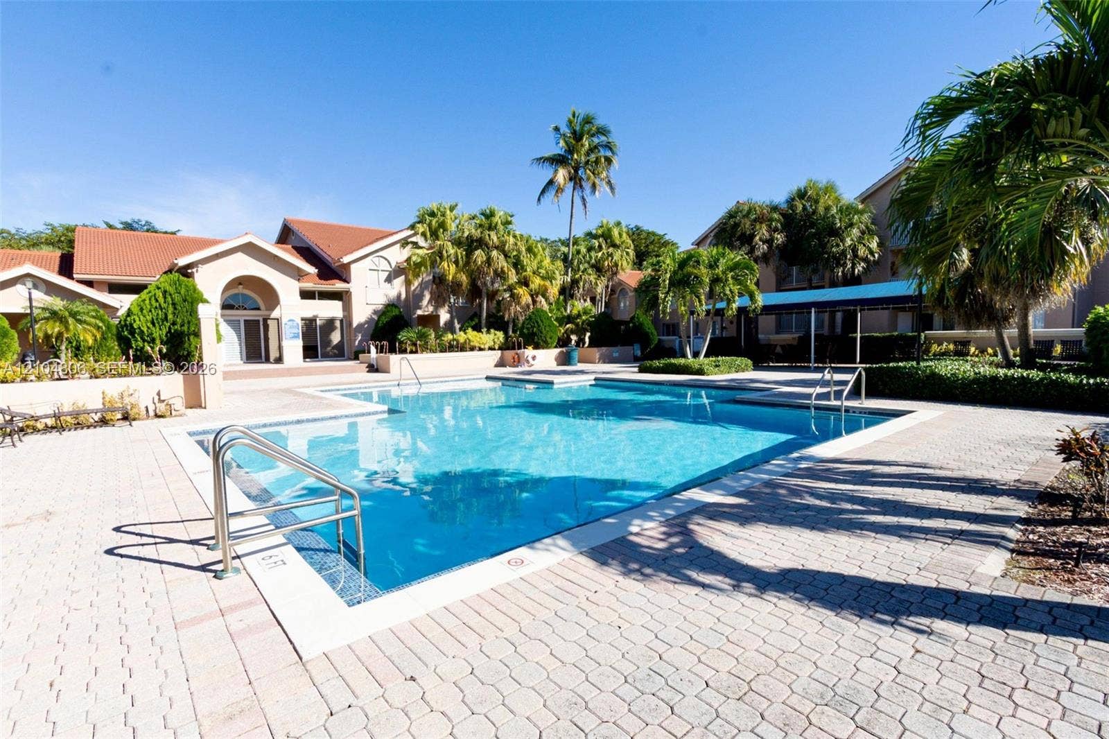 10451 SW 157th Place, #303, Miami, FL 33196 Resort-style swimming pool surrounded by paver patio and tropical landscaping, with community building featuring arched entryway