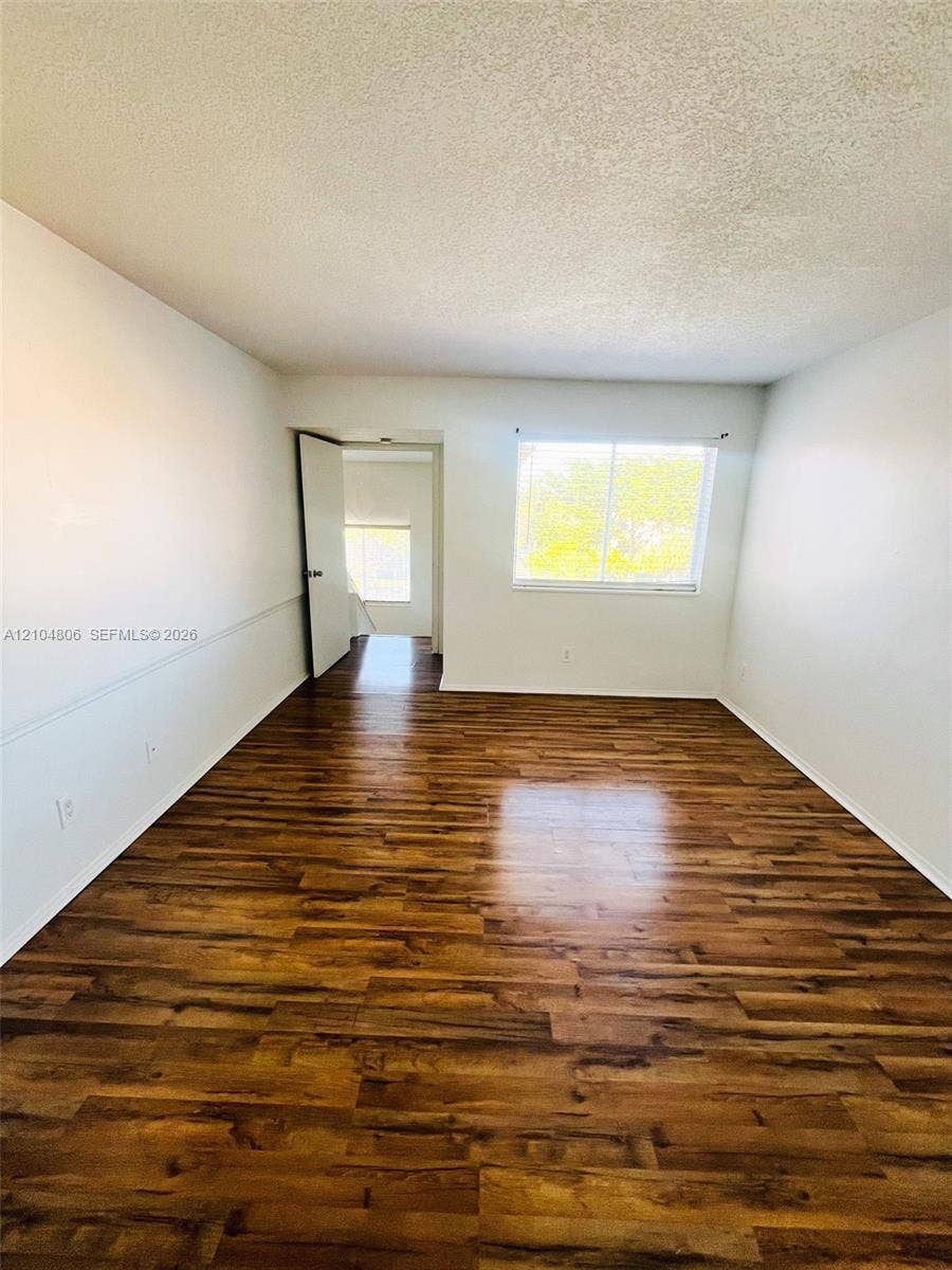 10451 SW 157th Place, #303, Miami, FL 33196 Wood-finish flooring, white wall paneling, and a large window with horizontal blinds