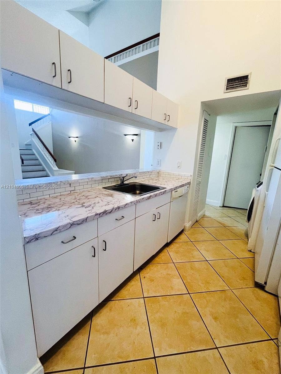 10451 SW 157th Place, #303, Miami, FL 33196 Kitchenette with white cabinetry and dark hardware, stone-finish countertops, ceramic tile backsplash, and a stainless steel sink