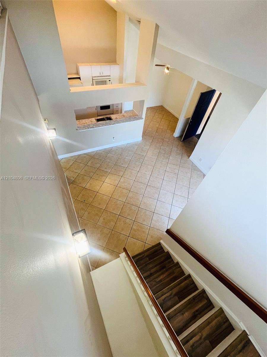 10451 SW 157th Place, #303, Miami, FL 33196 Two-story living space featuring a wood-finish staircase, tiled flooring, vaulted ceilings, a kitchen with built-in appliances, and a breakfast bar with stone-finish countertops