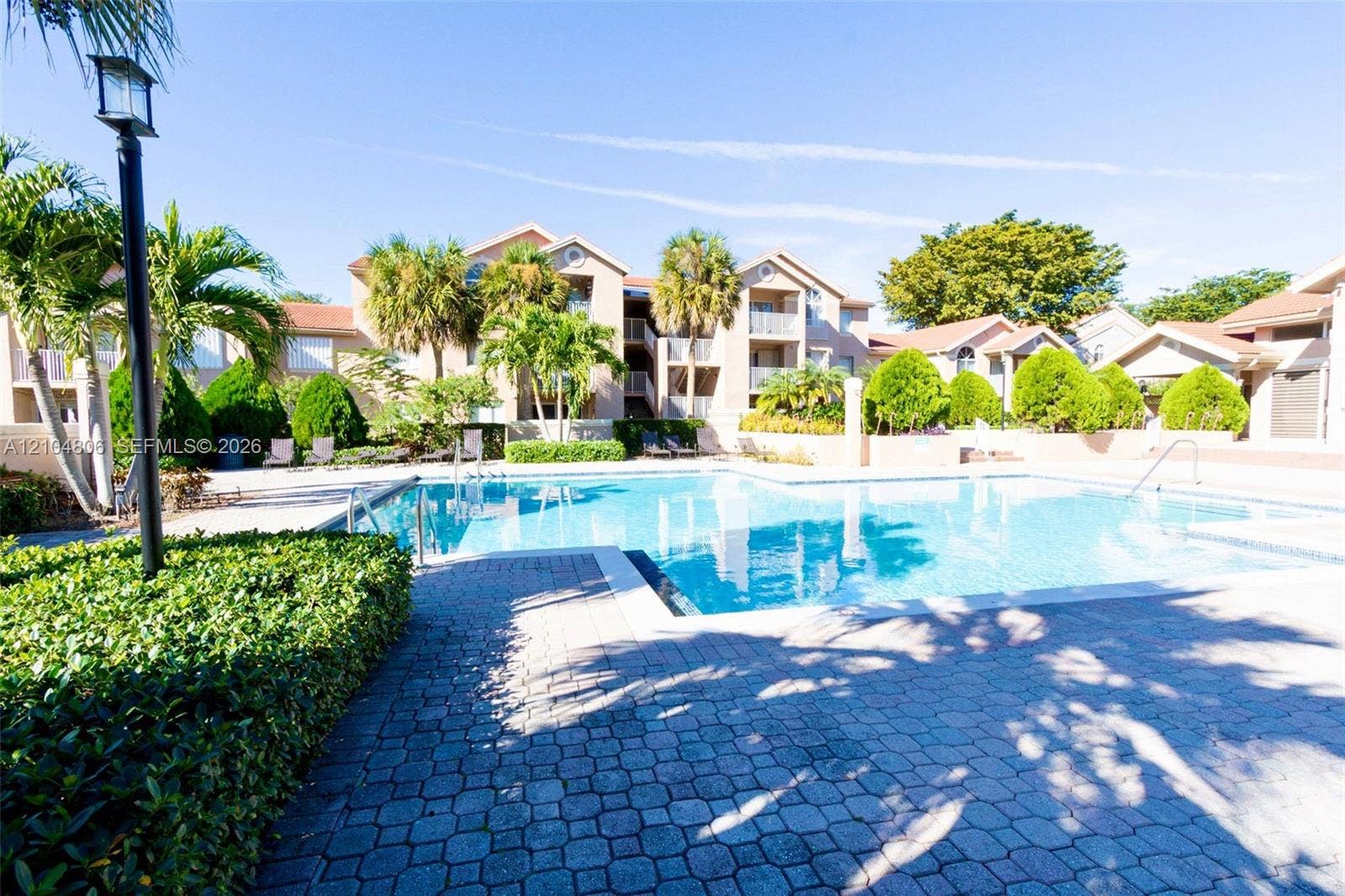 10451 SW 157th Place, #303, Miami, FL 33196 Expansive swimming pool with a paved deck, surrounded by mature landscaping, palm trees, and residential buildings