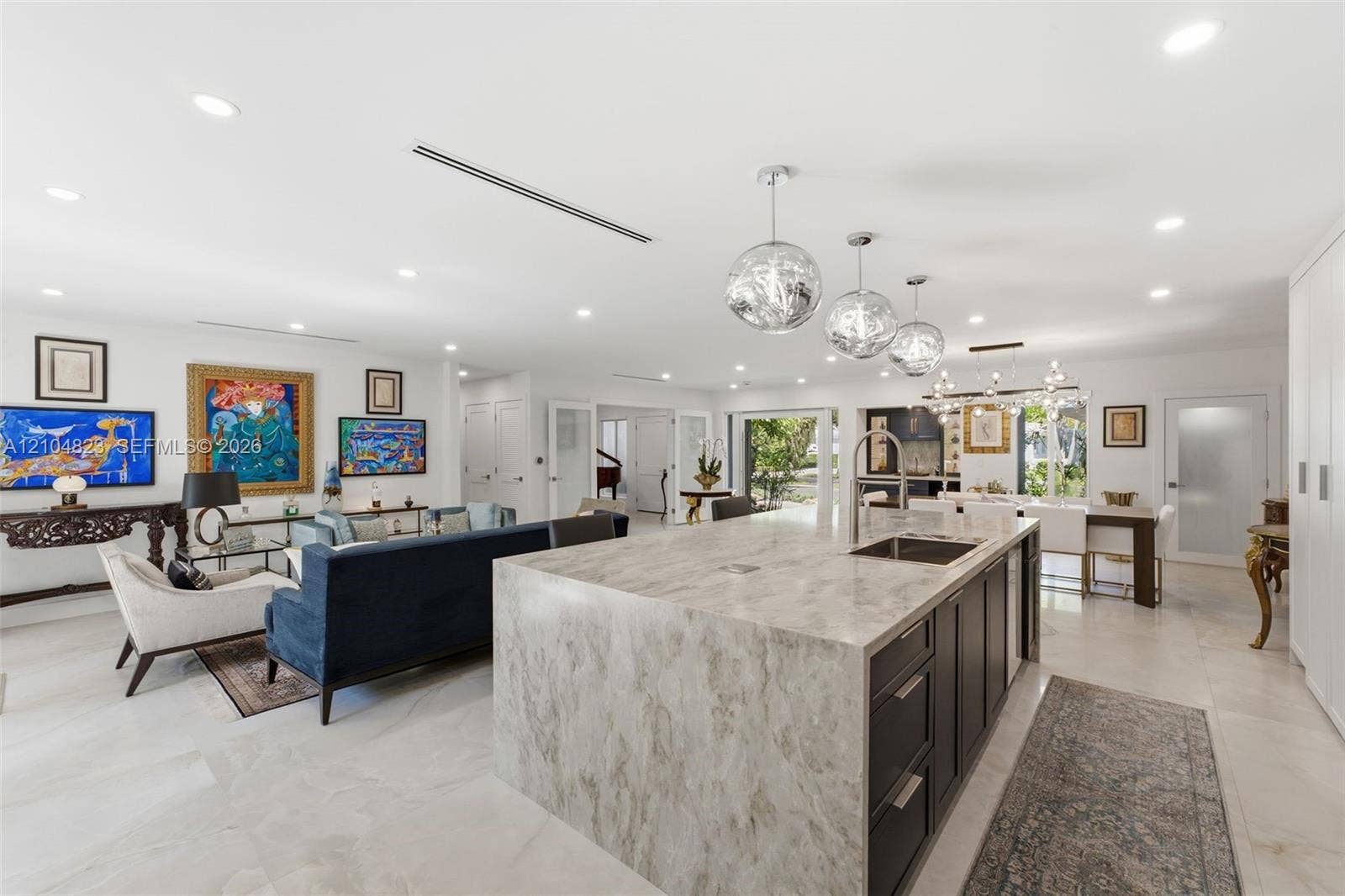 291 E Shore Drive E, Miami, FL 33133 Expansive open-concept living space featuring a large kitchen island with integrated sink, white tile flooring, recessed lighting, and multiple pendant light fixtures