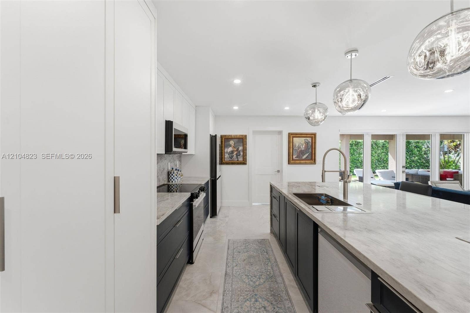 291 E Shore Drive E, Miami, FL 33133 Contemporary kitchen featuring an expansive island with an undermount sink, pendant lighting, built-in appliances, and white flat-panel cabinetry