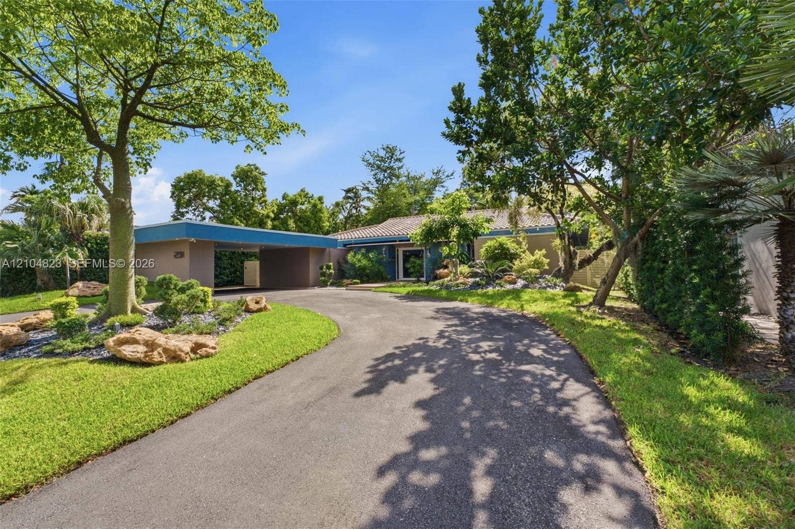 291 E Shore Drive E, Miami, FL 33133 Paved circular driveway leading to a covered carport, mature trees, manicured lawn, and established landscaping