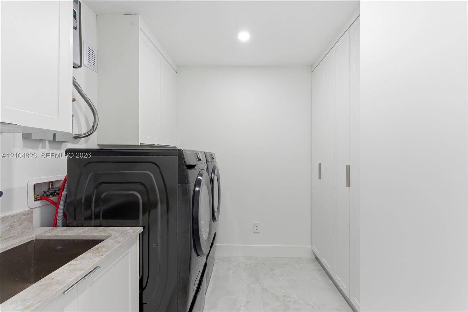 291 E Shore Drive E, Miami, FL 33133 Integrated laundry area featuring full-height white cabinetry, a utility sink with a stone-finish countertop, and recessed ceiling lighting