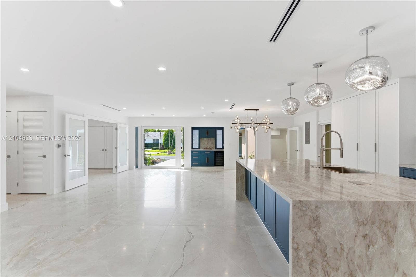 291 E Shore Drive E, Miami, FL 33133 Open-concept kitchen featuring an expansive waterfall-edge island, stone-finish countertops, custom cabinetry, recessed lighting, and glass pendant fixtures