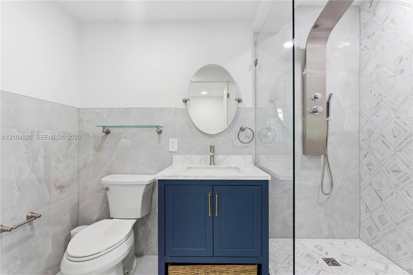 291 E Shore Drive E, Miami, FL 33133 White and grey tiled bathroom featuring a navy vanity with a white countertop, a frameless glass shower enclosure, and a modern shower panel system