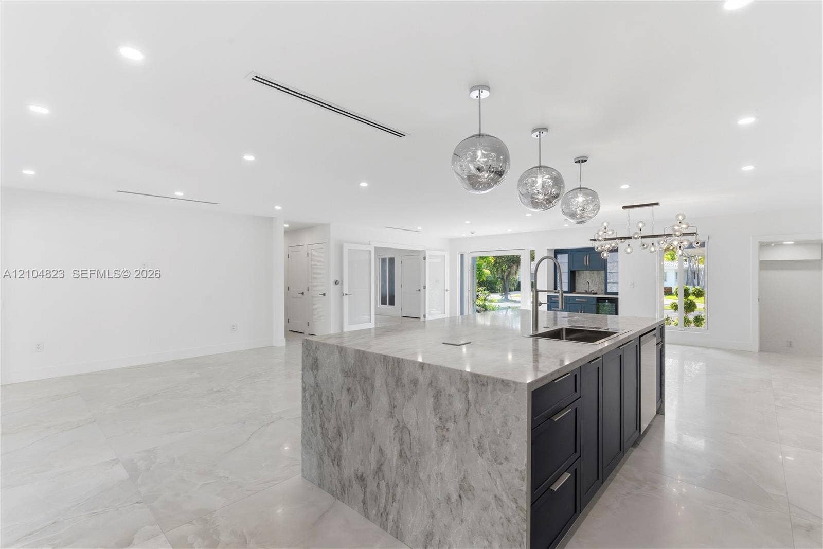 291 E Shore Drive E, Miami, FL 33133 Kitchen featuring a waterfall-edge island with stone-finish countertop, dark-toned cabinetry, recessed lighting, metallic pendant fixtures, and large-format tile flooring
