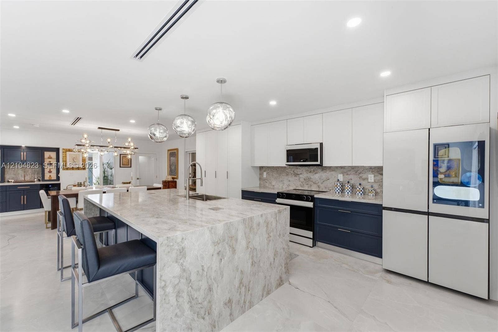 291 E Shore Drive E, Miami, FL 33133 Spacious kitchen featuring a large island with an undermount sink, pendant lighting, two-tone cabinetry, and an integrated refrigerator